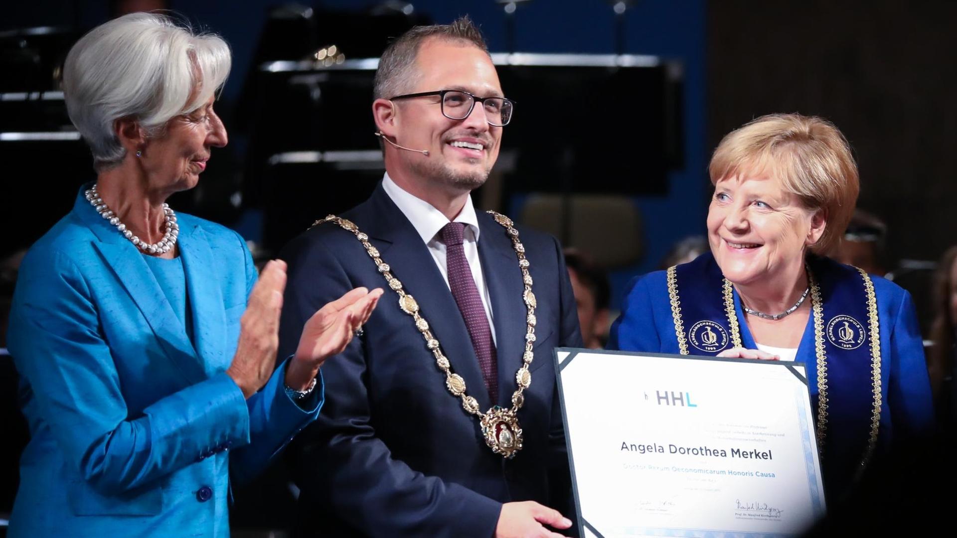 Christine Lagarde, designierte Präsidentin der Europäischen Zentralbank (EZB), Stephan Stubner, Rektor der Handelshochschule Leipzig (HHL), und Angela Merkel (CDU), Bundeskanzlerin stehen nebeneinander. Angela Merkel hält ihre Ehendoktor Urkunde in der Hand und lacht Lagarde an. Christine Lagarde, designierte Präsidentin der Europäischen Zentralbank (EZB), Stephan Stubner, Rektor der Handelshochschule Leipzig (HHL), und Angela Merkel (CDU), Bundeskanzlerin stehen nebeneinander. Angela Merkel hält ihre Ehendoktor Urkunde in der Hand und lacht Lagarde an.