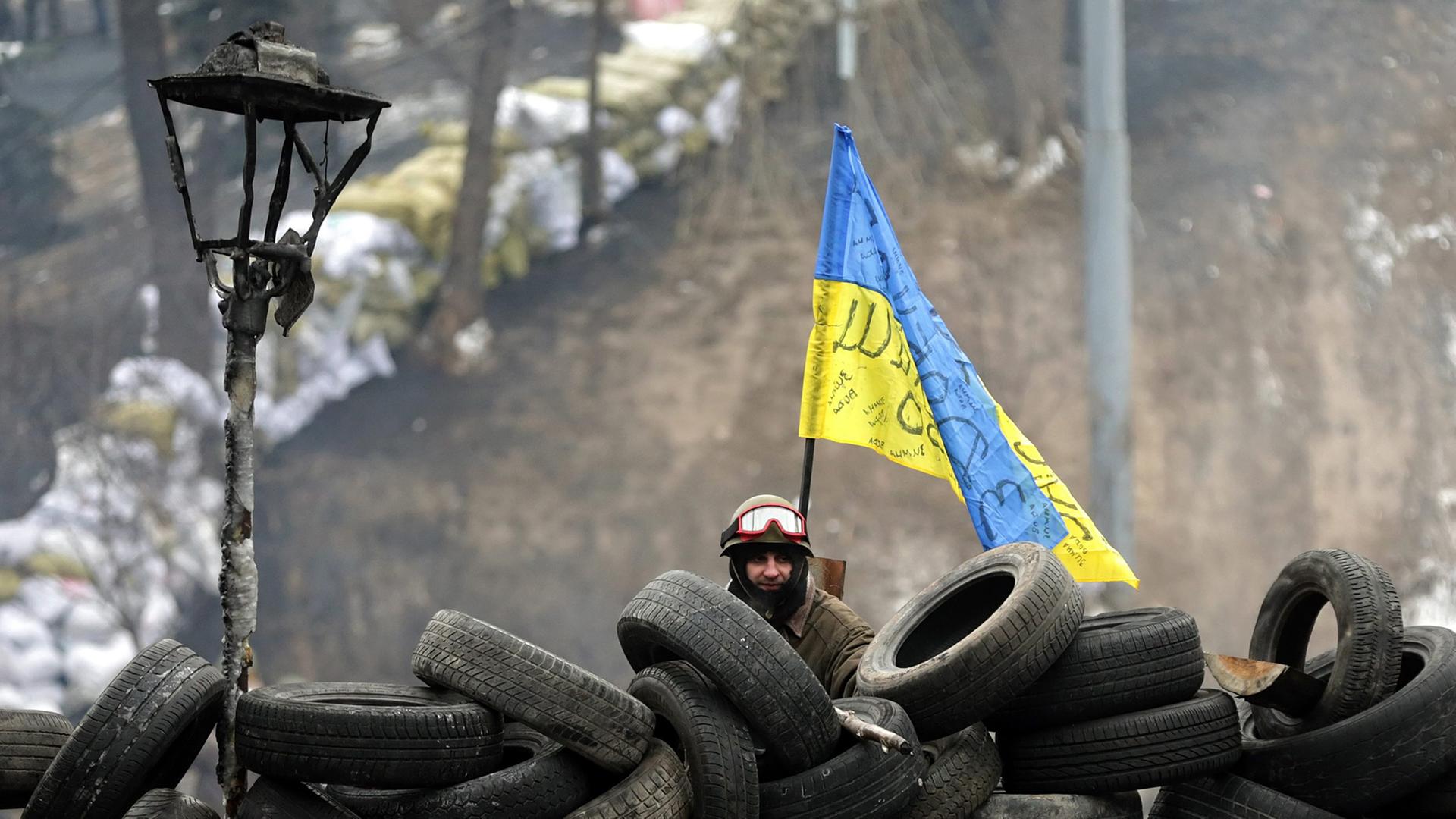 Ein Demonstrant steht in Kiew hinter einer Barrikade aus alten Autoreifen. Ein Demonstrant steht in Kiew hinter einer Barrikade aus alten Autoreifen.