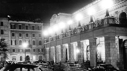 Historische Schwarz-weiß-Aufnahme der römischen Oper von 1951 im Dunklen, beleuchtet, vor dem Haus schwarze Autos.