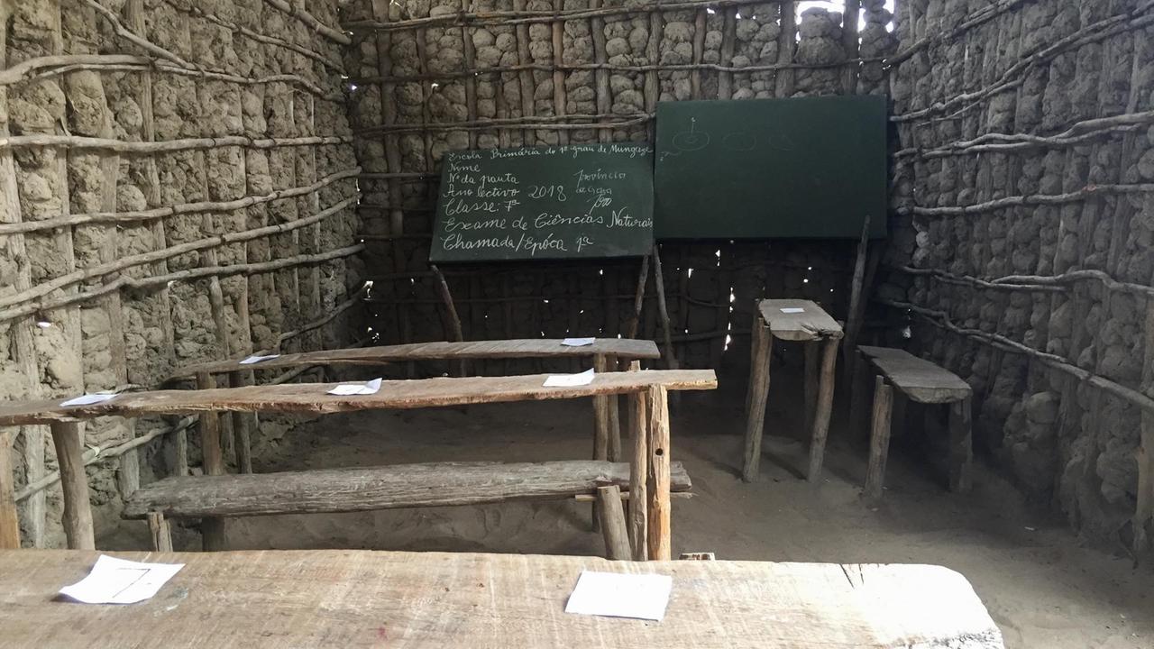 Blick in den Klassenraum der Dorfschule in Mungaze. Dort ist neben einfachen Tischen und Bänken aus Holz auch eine Tafel. Die Wände sind aus Lehm. 