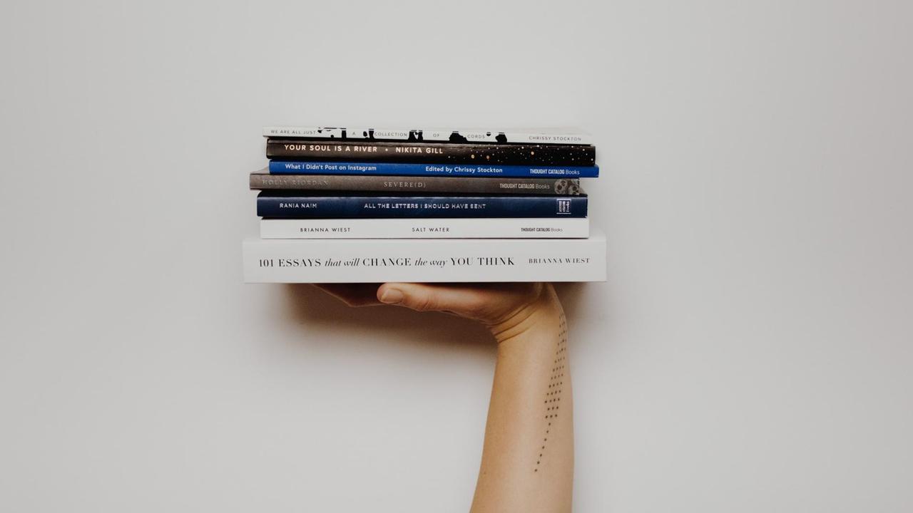 Eine Hand, nach oben gereckt, präsentiert einen Stapel Bücher auf der flachen Handfläche. Eine Hand, nach oben gereckt, präsentiert einen Stapel Bücher auf der flachen Handfläche.