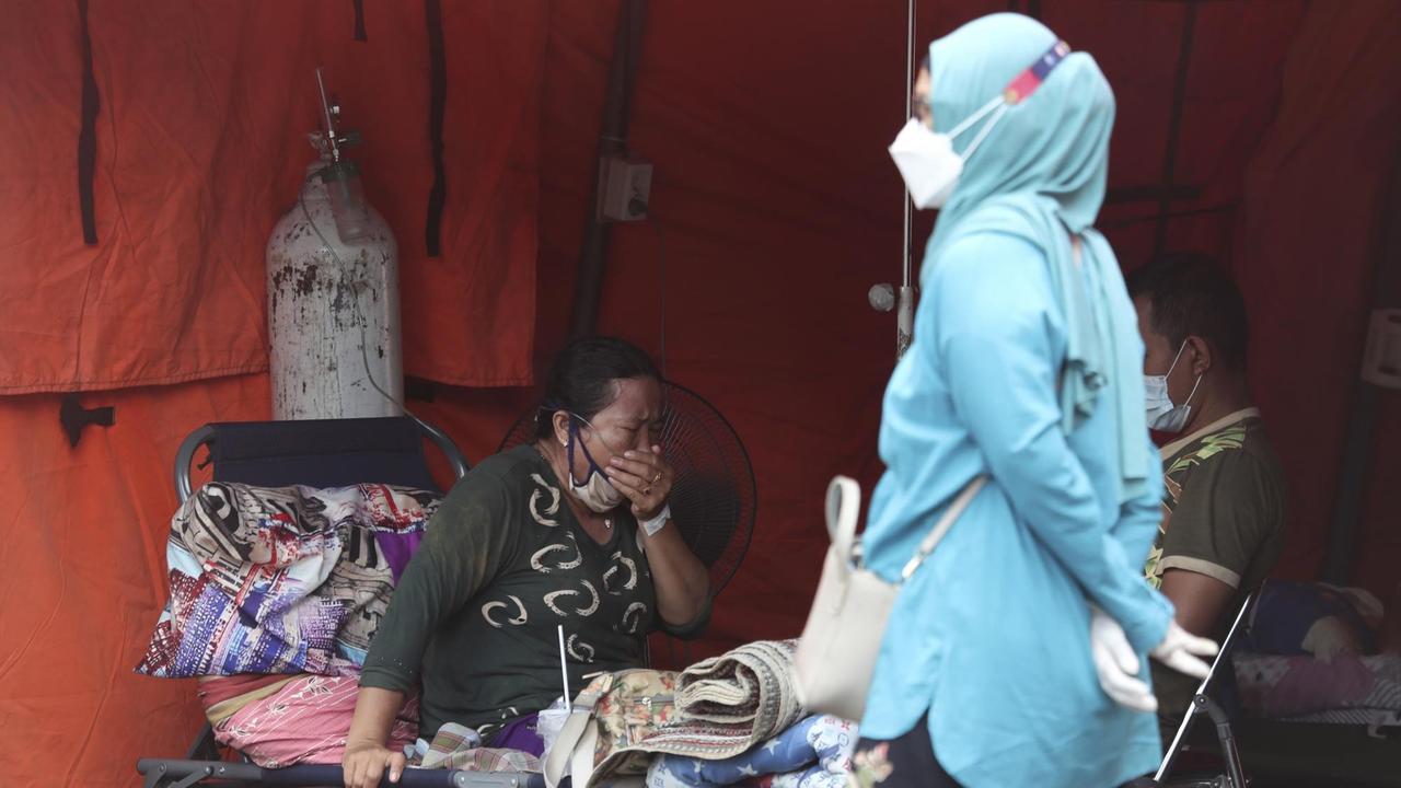 Indonesien, Bekasi: Eine Frau sitzt in einem Notfallzelt, das vor einem Krankenhaus errichtet wurde, um Corona-Patienten unterzubringen. Indonesien, Bekasi: Eine Frau sitzt in einem Notfallzelt, das vor einem Krankenhaus errichtet wurde, um Corona-Patienten unterzubringen.