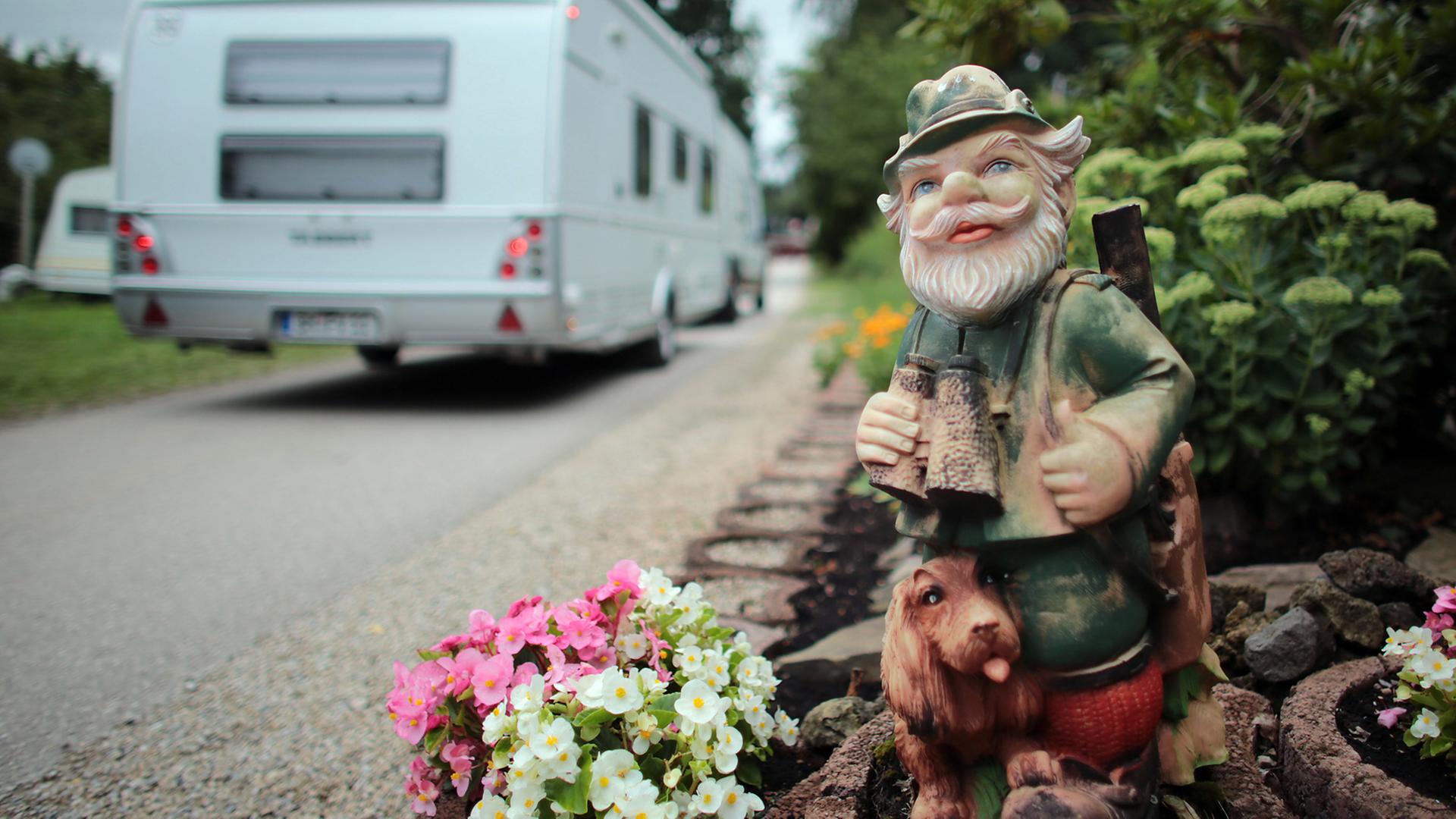 Ein Wohnwagen fährt auf einem Campingplatz an einem Gartenzwerg vorbei. Ein Wohnwagen fährt auf einem Campingplatz an einem Gartenzwerg vorbei.