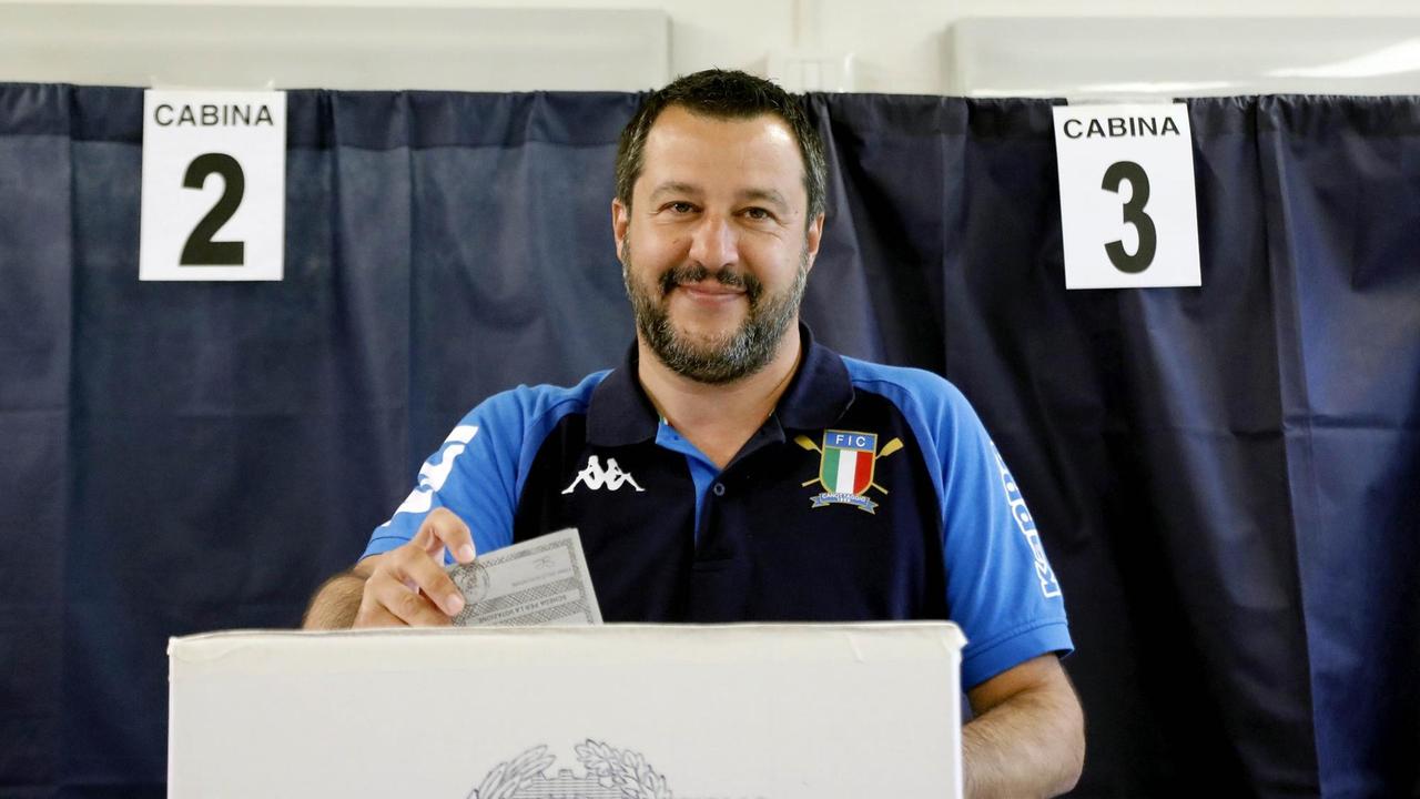 Matteo Salvini steckt seinen Stimmzettel in in eine Wahlurne. Im Hintergrund sind mehrere Kabinen mit Vorhängen zu sehen. Matteo Salvini steckt seinen Stimmzettel in in eine Wahlurne. Im Hintergrund sind mehrere Kabinen mit Vorhängen zu sehen.