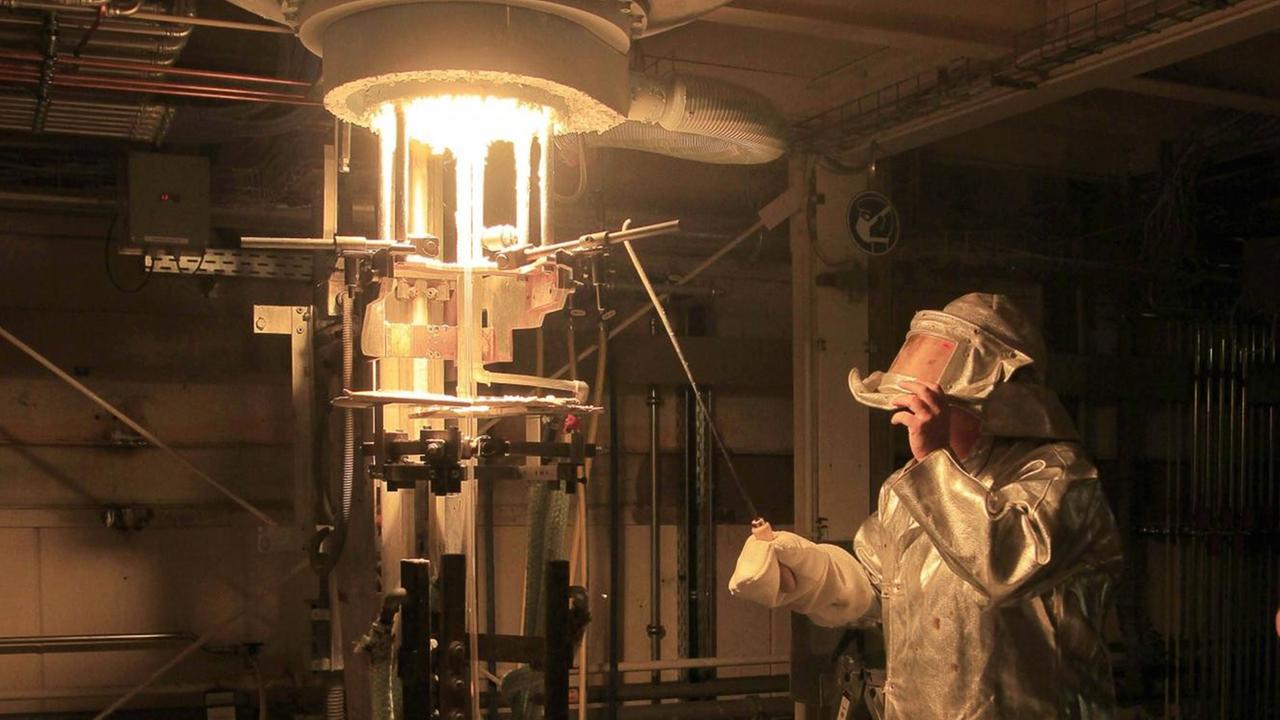 Ein Arbeiter kontrolliert Quarzglas, das aus dem Schmelztiegel des Ofens kommt Ein Arbeiter kontrolliert Quarzglas, das aus dem Schmelztiegel des Ofens kommt