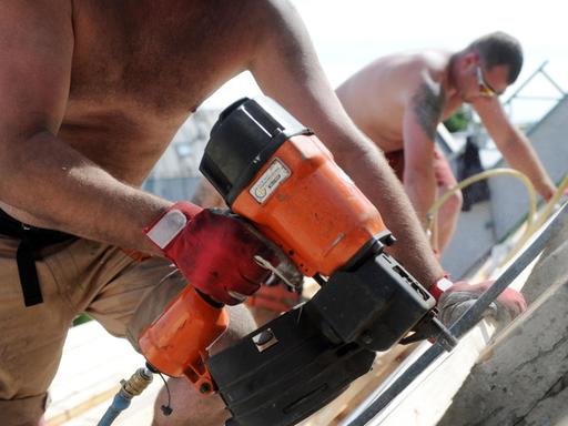 Bauarbeiter arbeiten mit nacktem Oberkörper in München auf einem Dach.