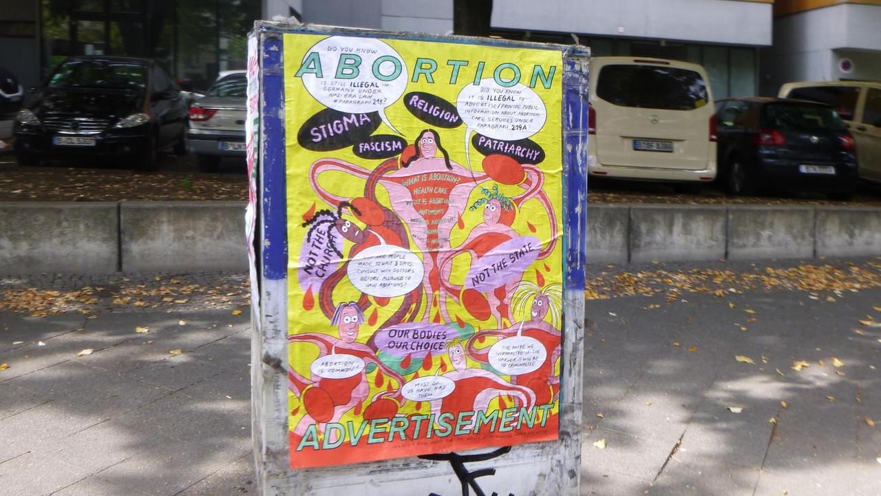 Am Stromkasten auf der Straße klebt ein Plakat. Auf dem illustrierten Motiv sind unter anderem die Wörter "Abortion" und "Adverstisesent" zu sehen. Am Stromkasten auf der Straße klebt ein Plakat. Auf dem illustrierten Motiv sind unter anderem die Wörter "Abortion" und "Adverstisesent" zu sehen.