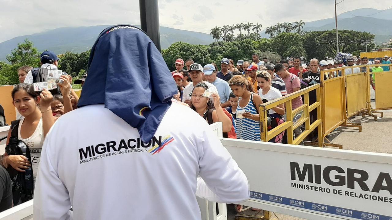 Ein Kontrolleur der Migrationsbehörde mit Sonnenschutz kontrolliert die Venezolaner, die ihre Dokumente hochhalten. Ein Kontrolleur der Migrationsbehörde mit Sonnenschutz kontrolliert die Venezolaner, die ihre Dokumente hochhalten.