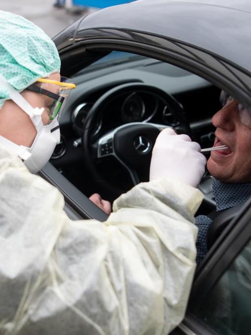 Eine Mitarbeiterin eines Krankenhauses nimmt während eines Pressetermins zum Start einer "Drive-In"-Teststation für den Coronavirus eine Probe durch ein Autofenster.