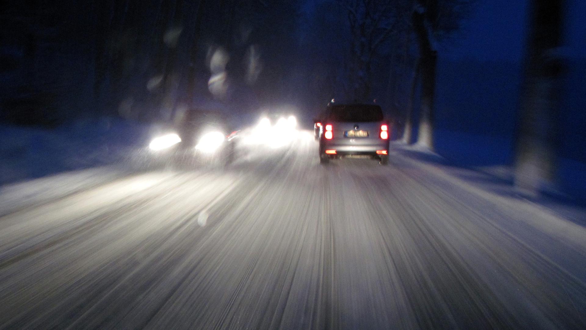 Blick durch eine Autoscheibe auf eine schneeglatte Straße im Dunkeln.