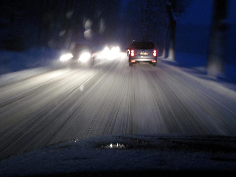 Blick durch eine Autoscheibe auf eine schneeglatte Straße im Dunkeln.