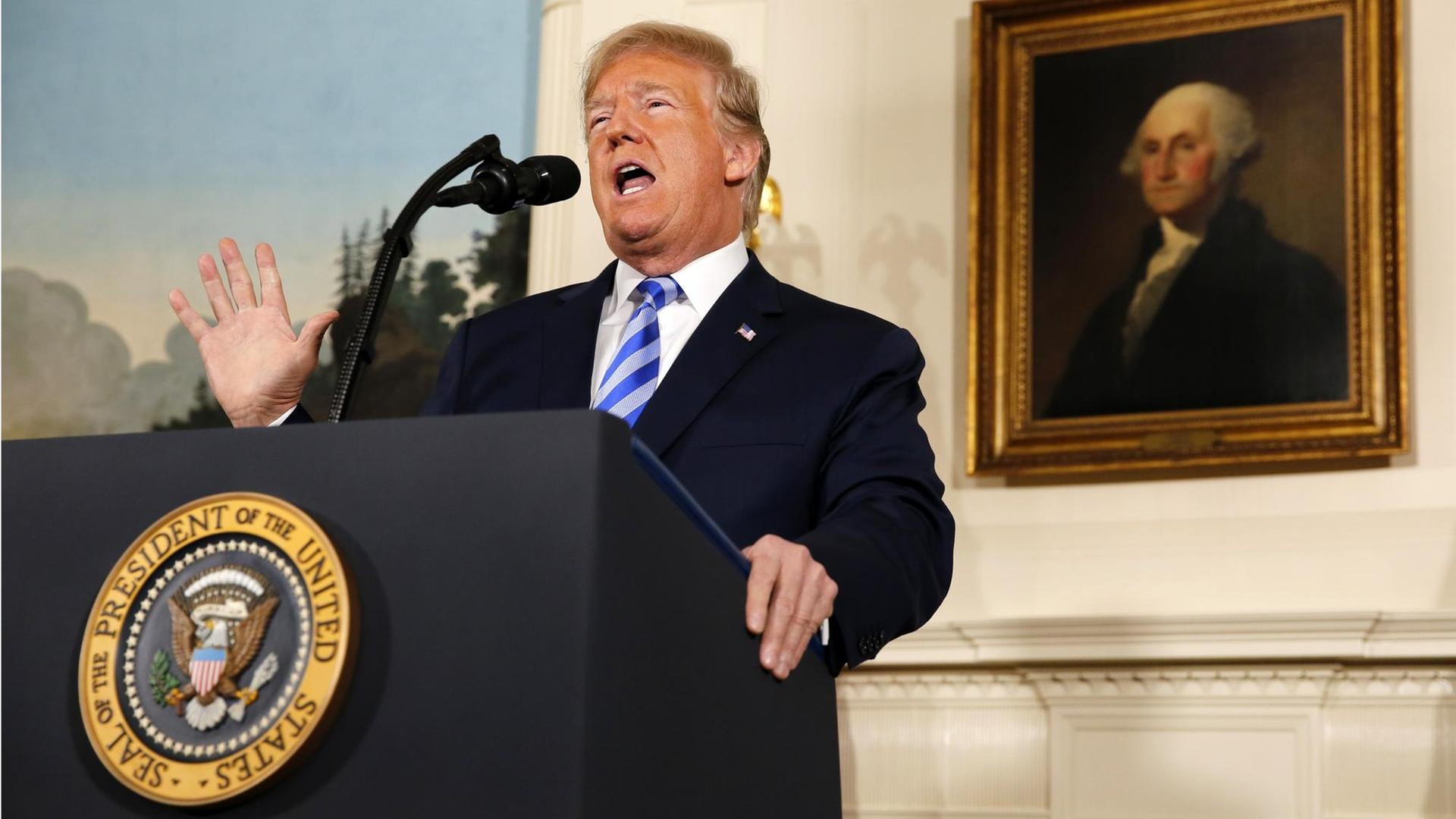 Präsident Donald Trump steht an einem Rednerpult. Die rechte Hand ist erhoben. Er verkündet das Ende des Atom-Deals mit dem Iran. Im Hintergrund ist ein Gemälde von George Washington zu sehen.
