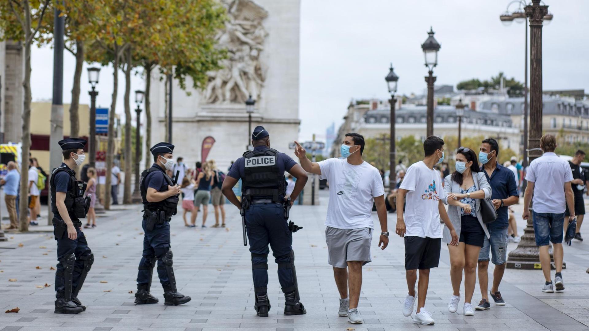Paris: Touristen mit Schutzmasken gehen auf der Prachtstraße Champs-Elysees an Polizisten vorbei. Paris: Touristen mit Schutzmasken gehen auf der Prachtstraße Champs-Elysees an Polizisten vorbei.