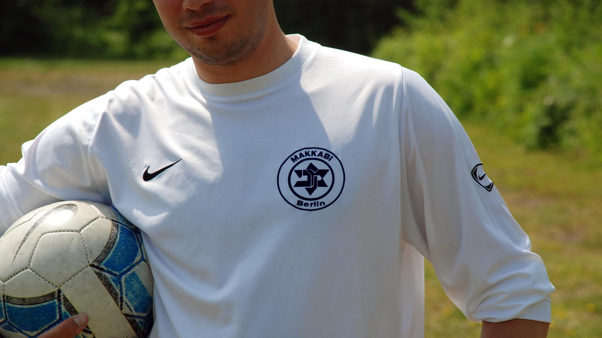 Ein Spieler von TuS Makkabi Berlin steht auf dem Spielfeld und hält den Ball unter dem Arm. Die Weiß-Blauen tragen auf ihrem Trikot einen verfremdeten Davidstern als Vereinswappen. (aufgenommen 2008) Ein Spieler von TuS Makkabi Berlin steht auf dem Spielfeld und hält den Ball unter dem Arm. Die Weiß-Blauen tragen auf ihrem Trikot einen verfremdeten Davidstern als Vereinswappen. (aufgenommen 2008)