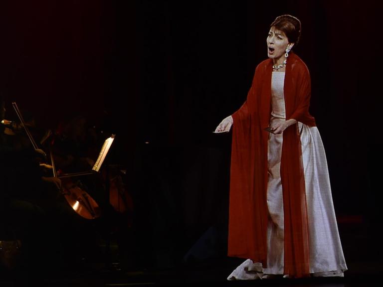 Ein dreidimensionales Hologramm, das aussieht wie die Opernsängerin Maria Callas steht vor einem Orchester und singt.