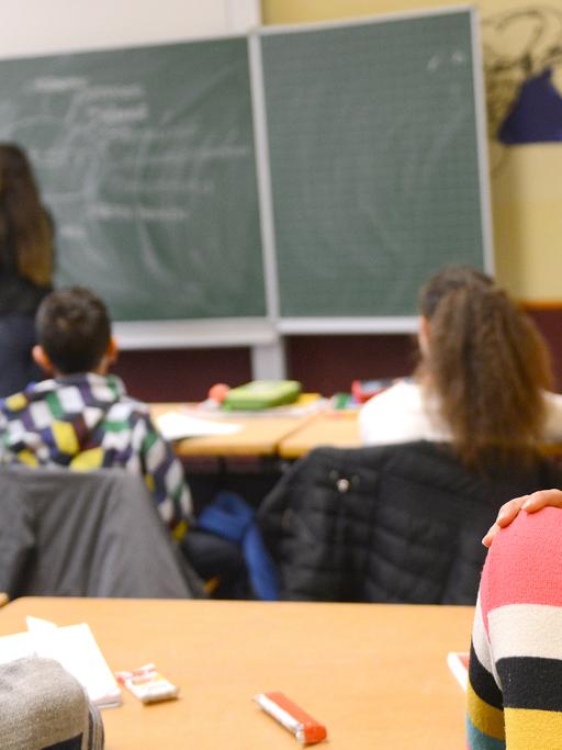 Kinder sitzen in einem Klassenraum und hören der Lehrerin zu.