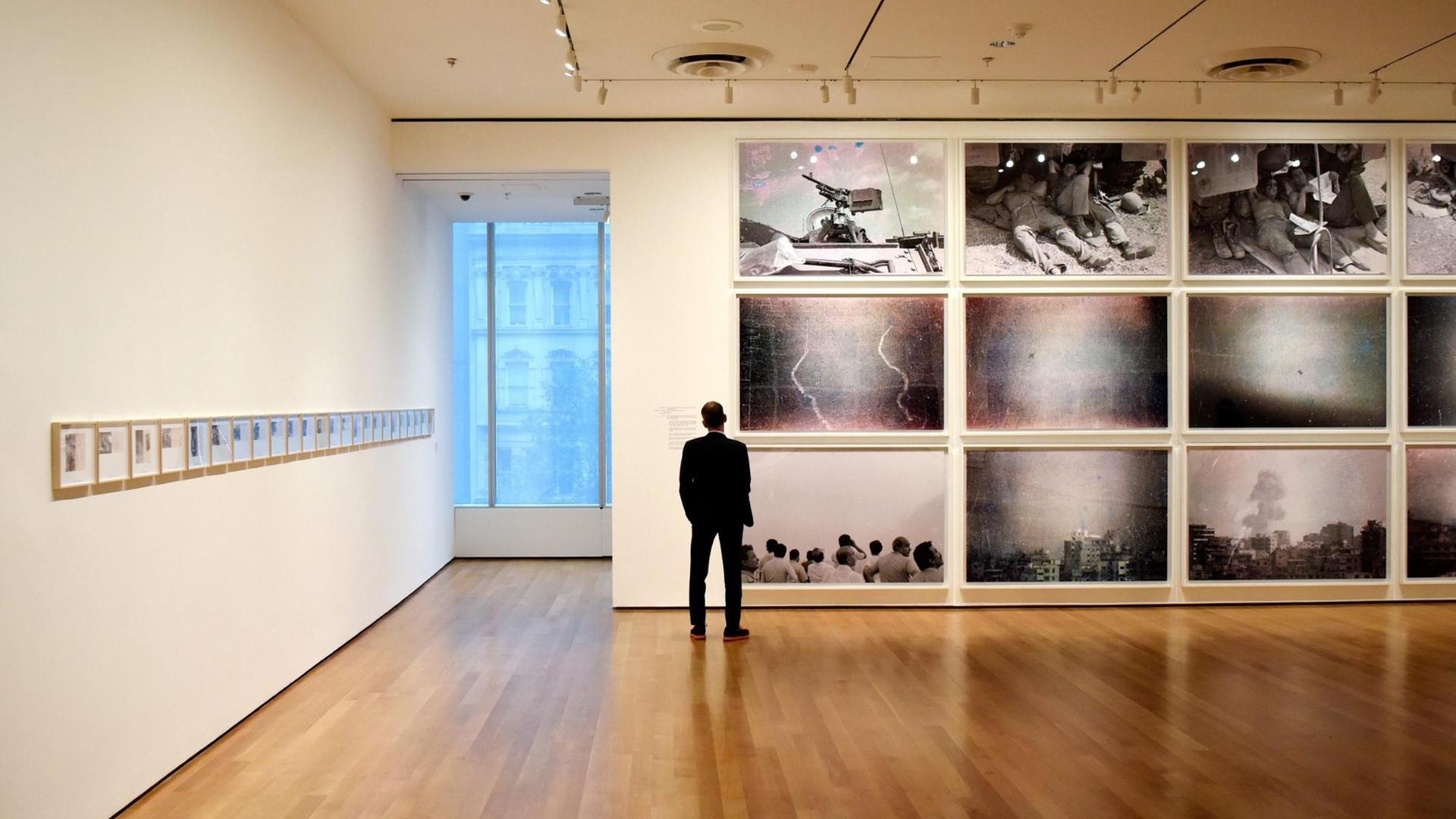 Ein Mann steht in einem Ausstellungsraum vor einer Wand und schaut sich Fotografien an. Ein Mann steht in einem Ausstellungsraum vor einer Wand und schaut sich Fotografien an.