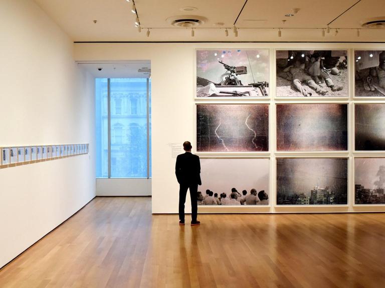 Ein Mann steht in einem Ausstellungsraum vor einer Wand und schaut sich Fotografien an.