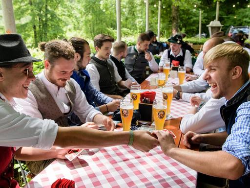 Eine Männergruppe spielt im Biergarten eines Wirtshauses an der Isar ein Kartenspiel.