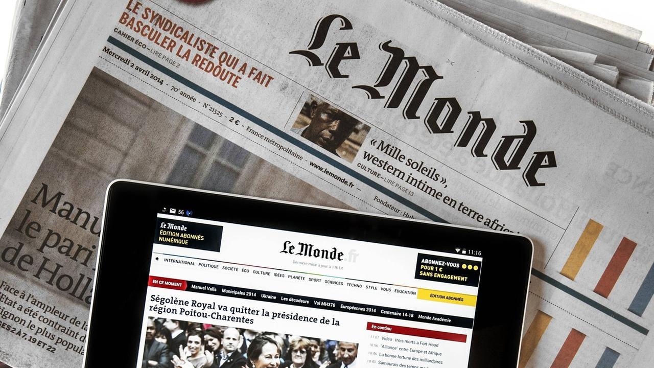 Das Touchscreen eines digitalen Tablets zeigt online Nachrichten, welches auf der französischen Zeitung "Le Monde" liegt.