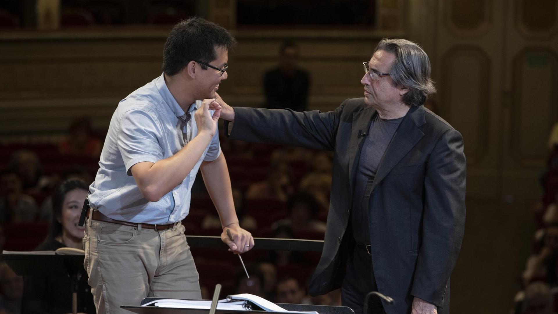 Riccardo Muti berührt die Schulter eines Nachwuchsdirigenten, der vor dem Dirigentenpult im Teatro Alighieri mit dem Luigi Cherubini Orchestra probt Riccardo Muti berührt die Schulter eines Nachwuchsdirigenten, der vor dem Dirigentenpult im Teatro Alighieri mit dem Luigi Cherubini Orchestra probt