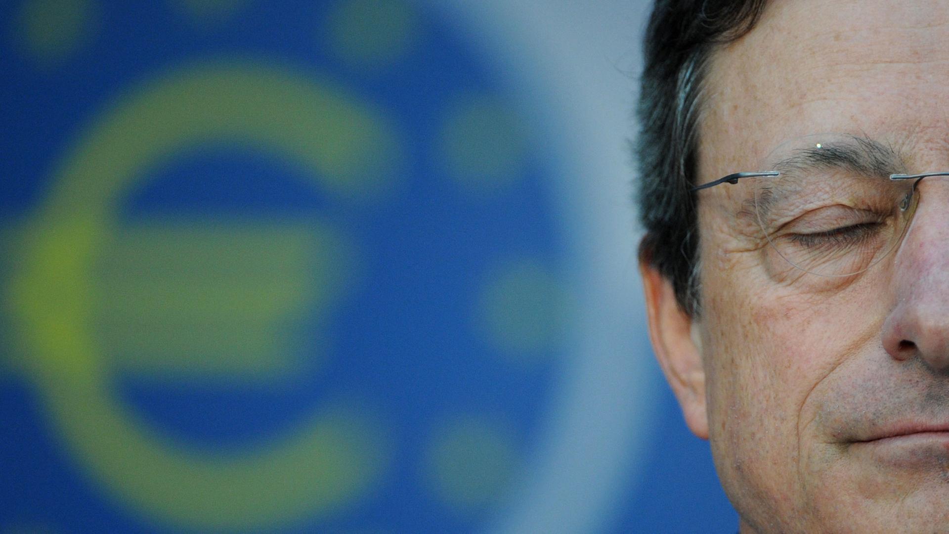 Mario Draghi hat die Augen geschlossen, im Hintergrund ist ein Eurozeichen zu sehen. Mario Draghi hat die Augen geschlossen, im Hintergrund ist ein Eurozeichen zu sehen.