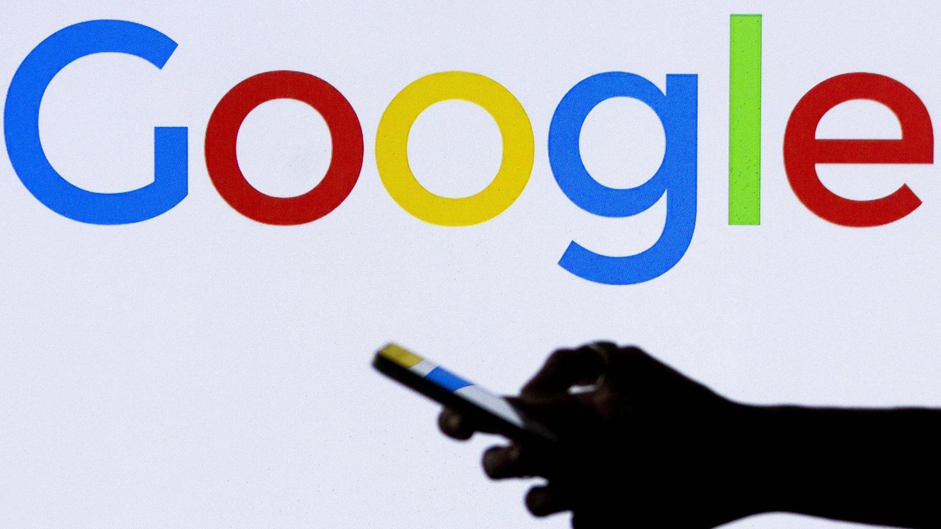 Hand mit Smartphone vor dem Logo von Google Hand mit Smartphone vor dem Logo von Google