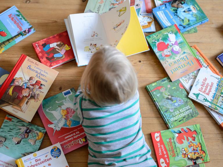 Ein Kind liegt zwischen vielen Büchern und schaut sich ein Buch an, aufgenommen am 28.01.2015 in Dresden (Sachsen).