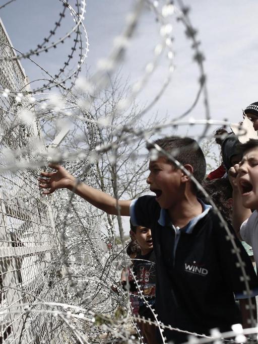 Flüchtlingskinder an einem mit Stacheldraht ausgestatteten Zaun an der griechisch-mazedonischen Grenze im Lager Idomeni.