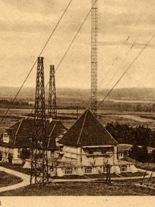 Eine historische Postkarte zeigt einige Gebäude, zwischen denen hohe Masten stehen, die über lang gespannte Seile gesichert sind.
