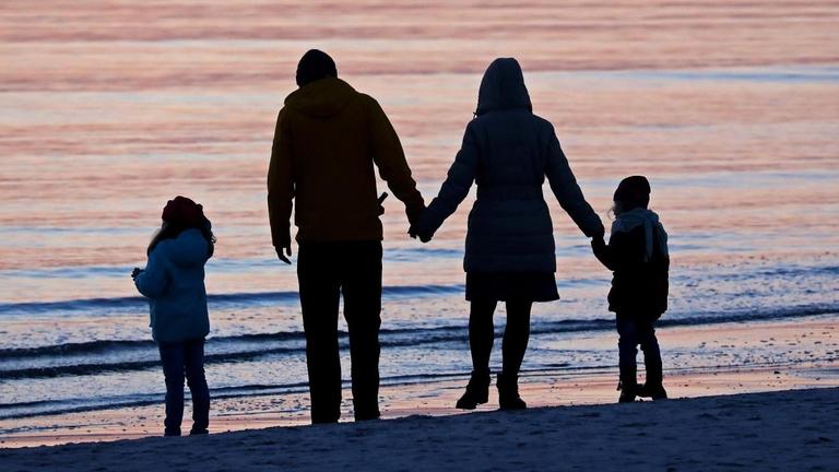 Eine Familie ist im Licht der untergehenden Sonne an der Ostsee auf der Insel Hiddensee bei Vitte (Mecklenburg-Vorpommern) unterwegs.