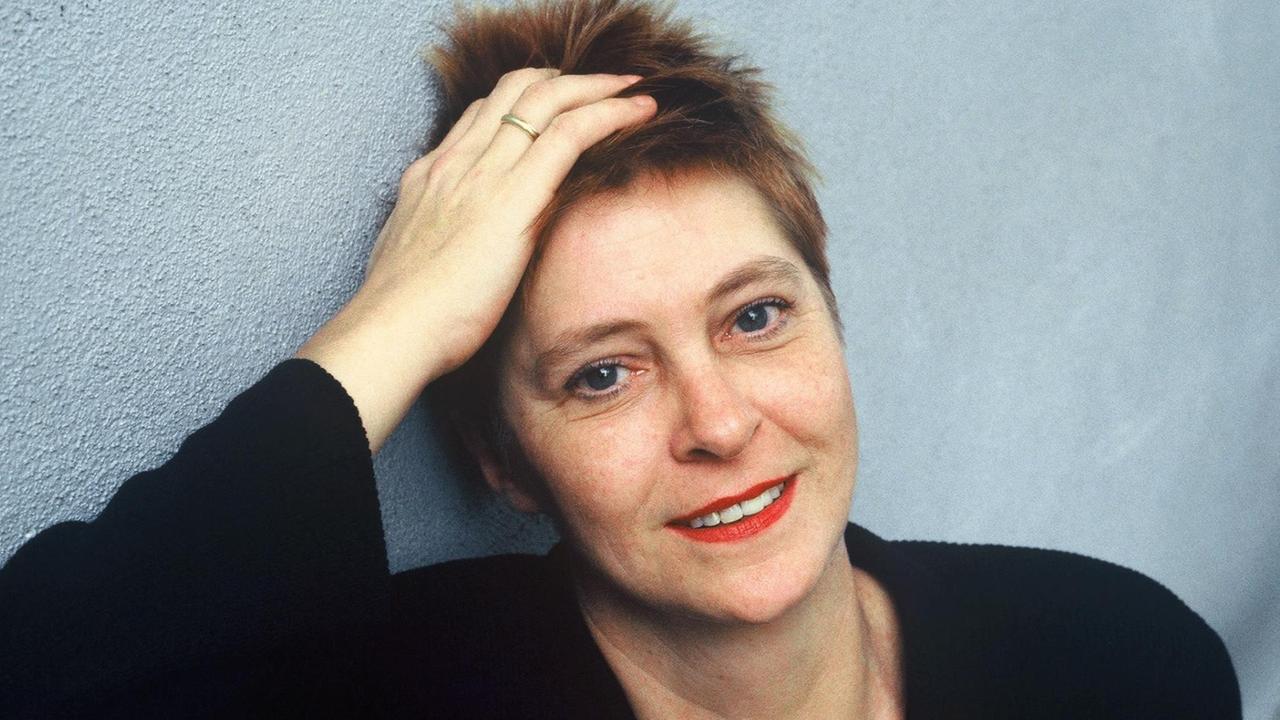 Pieke Biermann, rötliche kurze Haare, roter Lippenstift und schwarzes Oberteil, lehnt ihren Kopf vor hellblauem Hintergrund an der rechten Hand an. Pieke Biermann, rötliche kurze Haare, roter Lippenstift und schwarzes Oberteil, lehnt ihren Kopf vor hellblauem Hintergrund an der rechten Hand an.