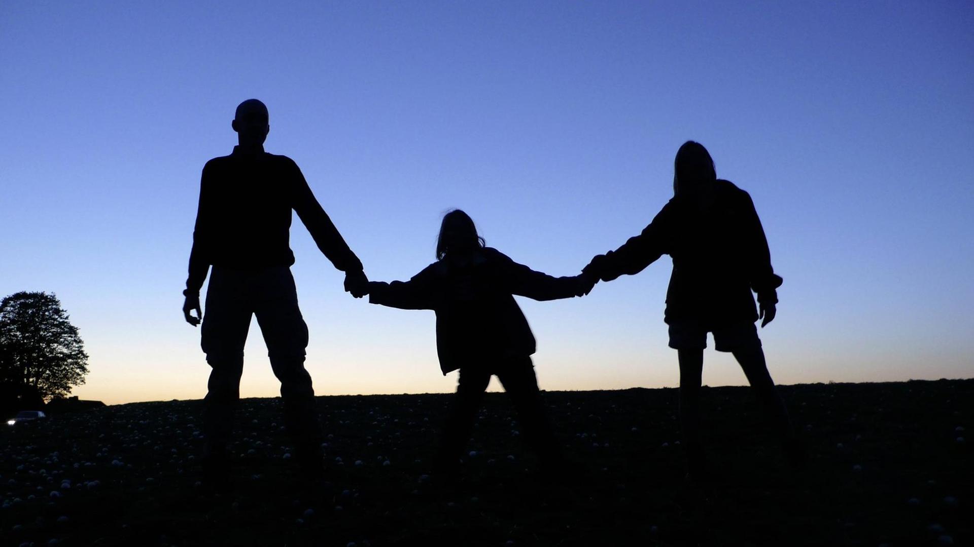 Schattenriss , Eltern mit Kind. Das Kind ist in der Mitte und wird an beiden Armen von jeweils einem Elternteil gehalten Schattenriss , Eltern mit Kind. Das Kind ist in der Mitte und wird an beiden Armen von jeweils einem Elternteil gehalten
