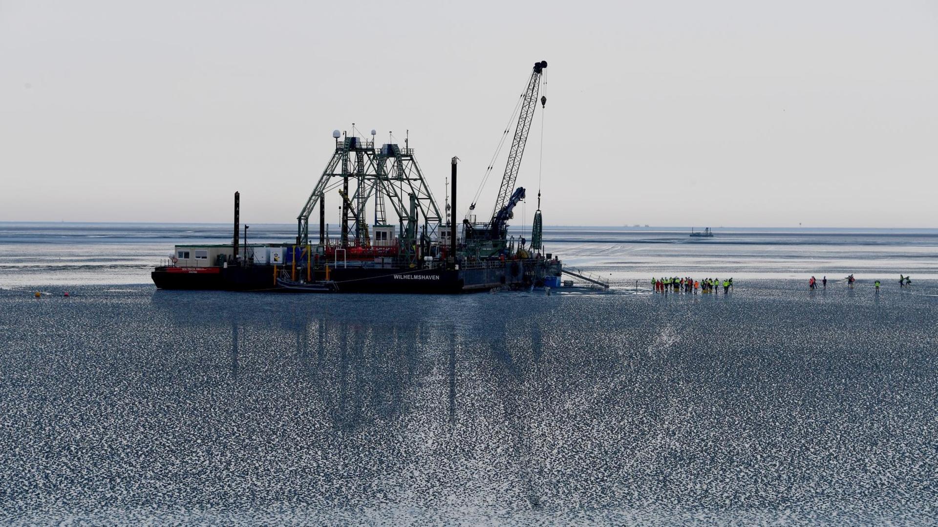 Das Endstück eines Seekabels wird von dem Kabelverlegeschiff "Boka Connector" im Watt unter dem Deich hindurch an Land gezogen. Das Endstück eines Seekabels wird von dem Kabelverlegeschiff "Boka Connector" im Watt unter dem Deich hindurch an Land gezogen.