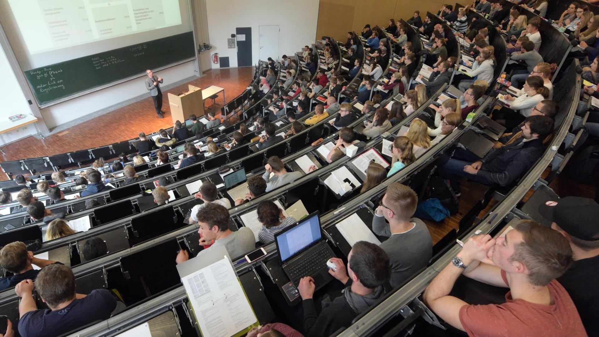 Totale von oben auf den Hörsaal mit Studierenden und dem Dozenten am Pult Totale von oben auf den Hörsaal mit Studierenden und dem Dozenten am Pult