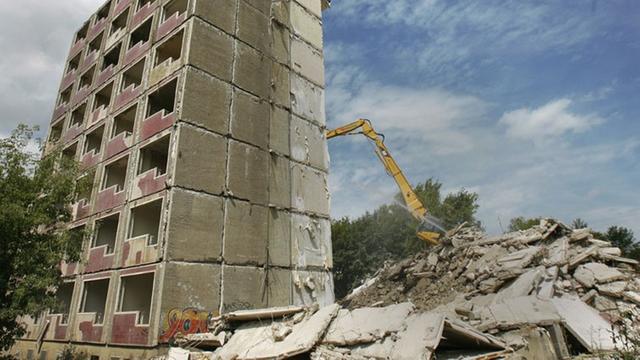 Ein Bagger reißt einen Plattenbau ein.