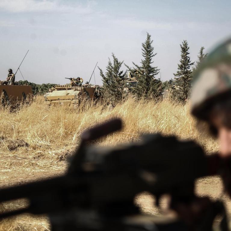 Ein von der Türkei unterstützte Rebell der Syrischen Nationalarmee richtet seine Waffe aus, während im Hintergrund türkische Panzer vorbeifahren