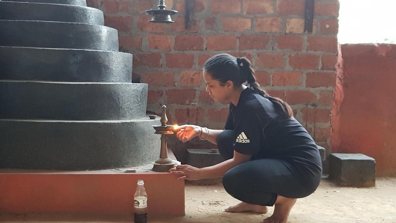 Eine junge Frau in Sportkleidung kniet vor einem Schrein in Form einer runden Pyramide und entzündet eine Kerze. Eine junge Frau in Sportkleidung kniet vor einem Schrein in Form einer runden Pyramide und entzündet eine Kerze.