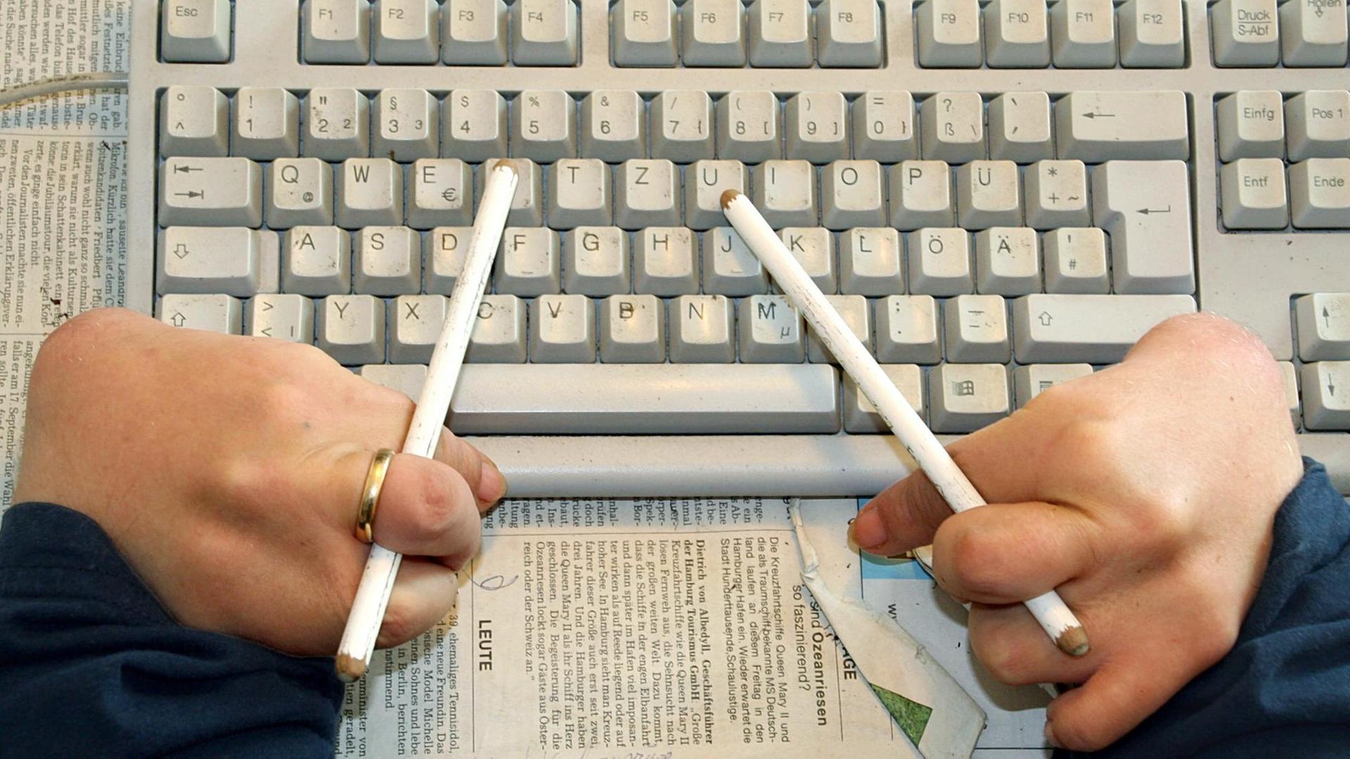 Ein Contergangeschädigter benutzt Radierstifte, um mit der Tastatur seines Computers zu arbeiten. Ein Contergangeschädigter benutzt Radierstifte, um mit der Tastatur seines Computers zu arbeiten.