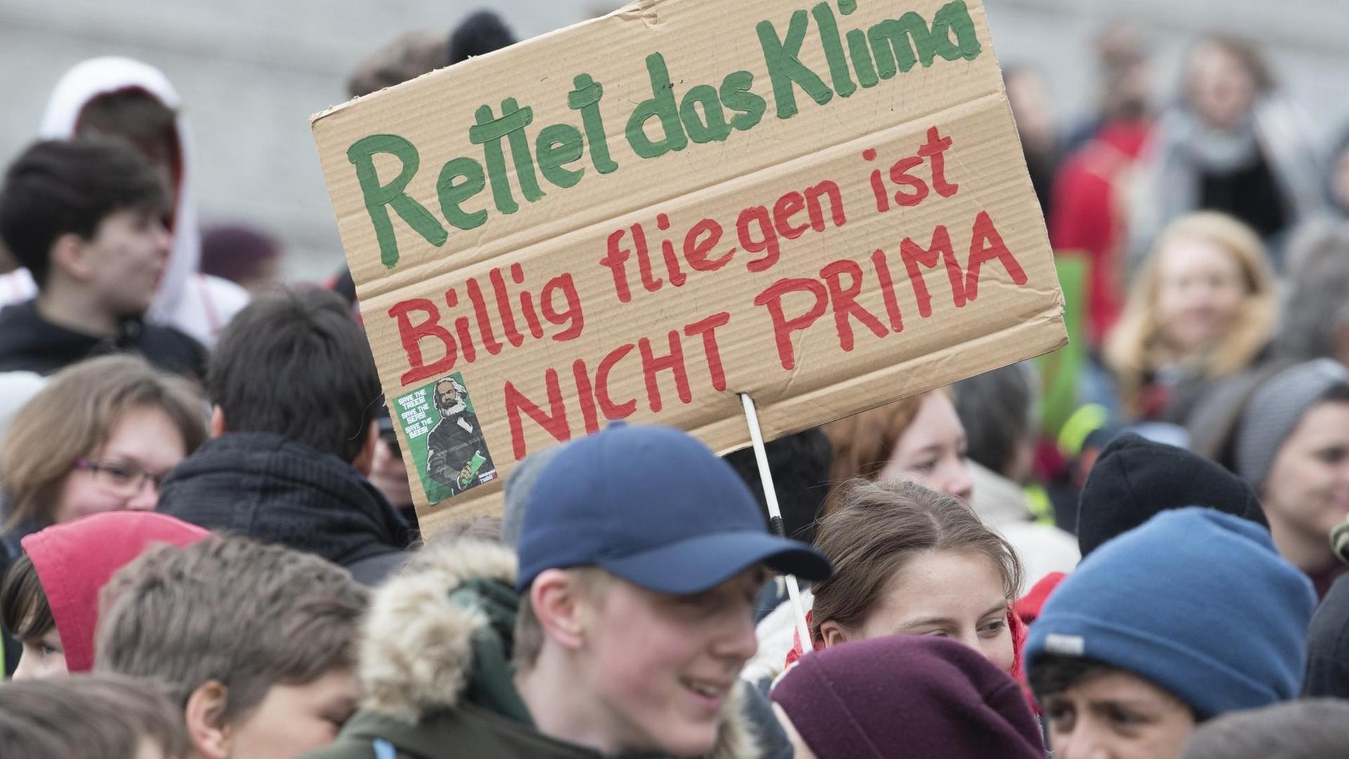 Teilnehmer*innen an der "Fridays for Future"-Klimastreikdemo halten Plakate, u.a. mit der Aufschrift "Rettet das Klima, Billig fliegen ist nicht prima". Teilnehmer*innen an der "Fridays for Future"-Klimastreikdemo halten Plakate, u.a. mit der Aufschrift "Rettet das Klima, Billig fliegen ist nicht prima".
