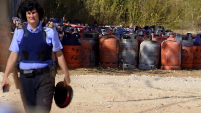 Eine Polizistin geht links aus dem Bild, im Hintergrund zahlreiche Gasflaschen. Das Foto zeigt den Ort Alcanar, wo sich am 16. August - einen Tag vor den Anschlägen in Spanien - eine Explosion ereignete.