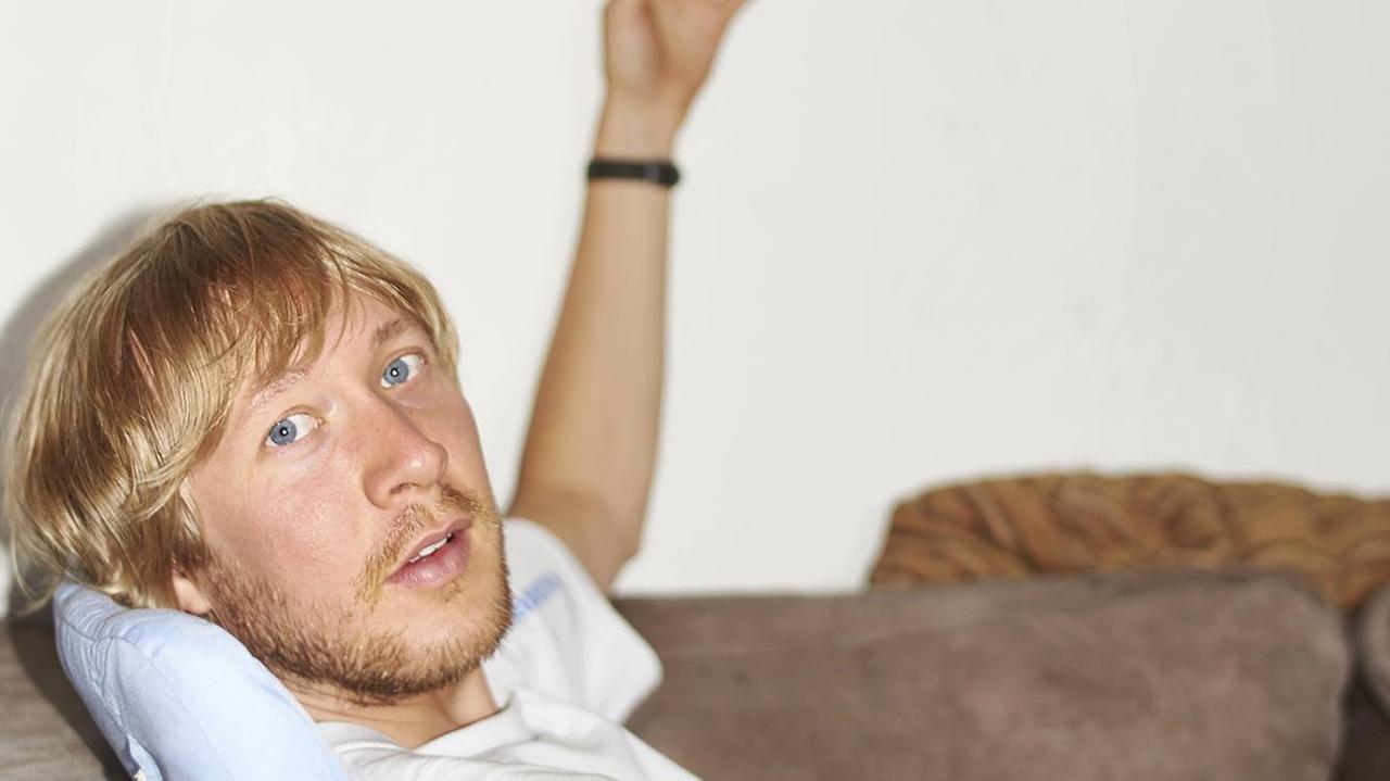 Der bildende Künstler Malte Bartsch liegt auf einem Sofa und guckt in die seitlich in die Kamera Der bildende Künstler Malte Bartsch liegt auf einem Sofa und guckt in die seitlich in die Kamera