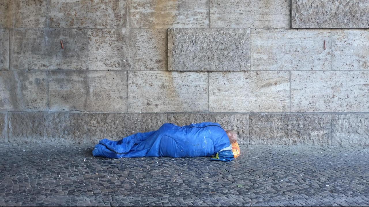 Ein Mann schläft in seinem blauen Schlafsack unter der S-Bahnbrücke an der Kantstraße im Berliner Bezirk Charlottenburg.