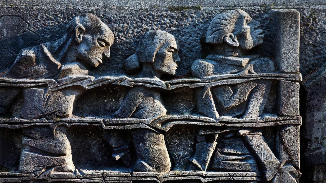 Das Mahnmal aus Stein zeigt drei Figuren hinter Stacheldraht. Das Mahnmal aus Stein zeigt drei Figuren hinter Stacheldraht.