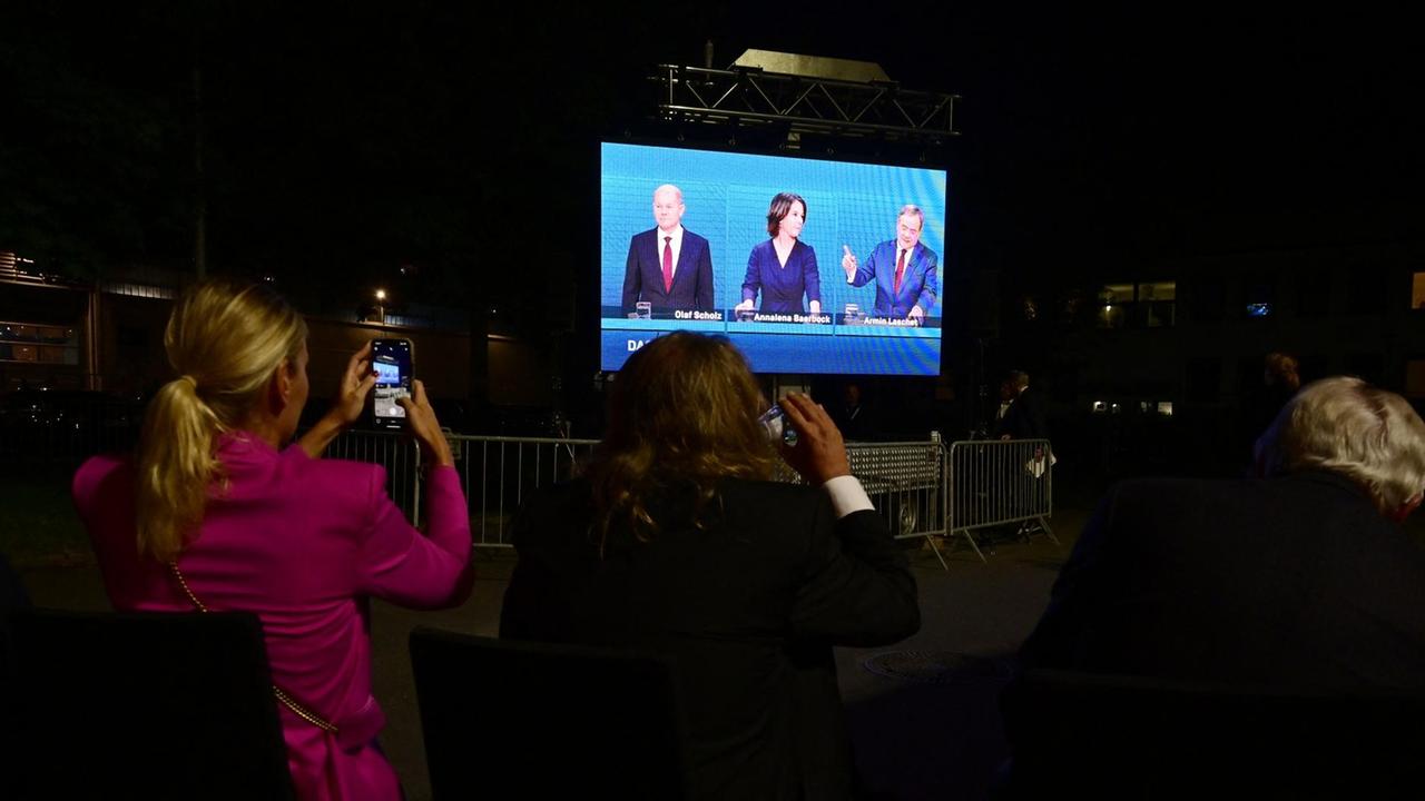 Zuschauerinnen filmen mit dem Smartphone eine Leinwand, auf der das TV-Triell der drei Kanzlerkandidaten übertragen wird.
