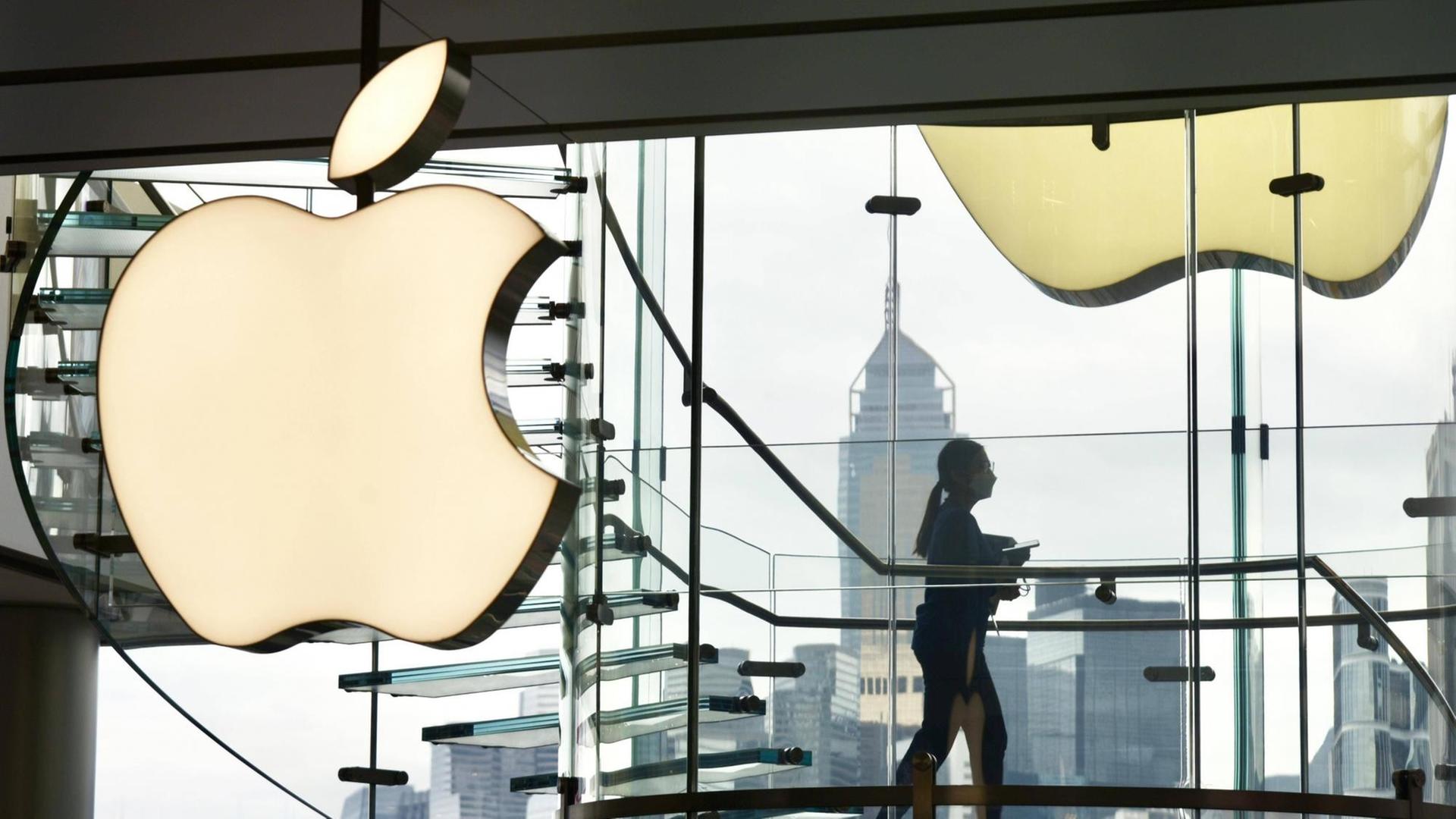 Eine Frau läuft in einem gläsernen treppenhaus an einem leuchtenden Apple-Logo vorbei. Eine Frau läuft in einem gläsernen treppenhaus an einem leuchtenden Apple-Logo vorbei.