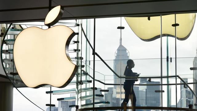 Eine Frau läuft in einem gläsernen treppenhaus an einem leuchtenden Apple-Logo vorbei.