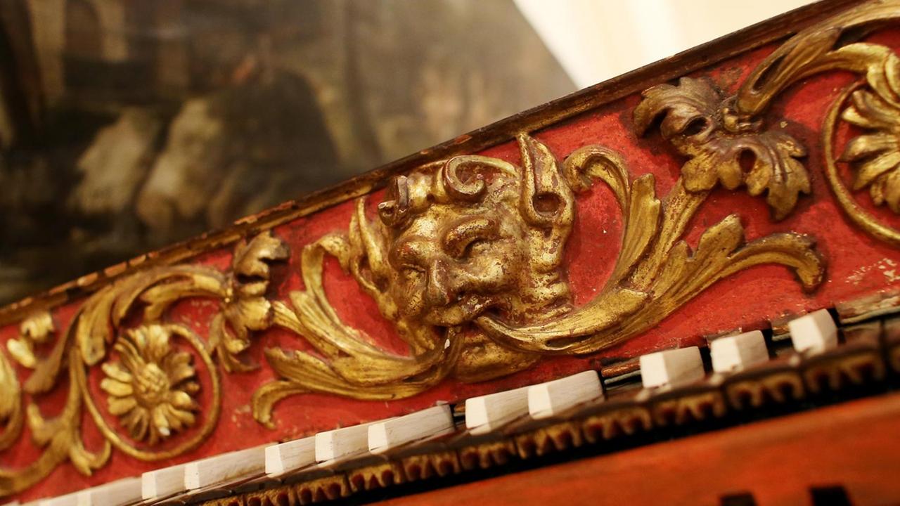 Detailansicht eines Cembalos mit goldenen Verzierungen, schwarzen und weißen Tasten und üppigem rot-goldenen Holzschmuck am Instrument. Detailansicht eines Cembalos mit goldenen Verzierungen, schwarzen und weißen Tasten und üppigem rot-goldenen Holzschmuck am Instrument.