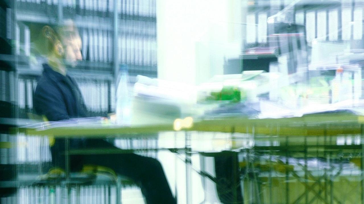 Ein Mann sitzt abends in einem Büro an einem vollen Schreibtisch und arbeitet in Berlin. Ein Mann sitzt abends in einem Büro an einem vollen Schreibtisch und arbeitet in Berlin.
