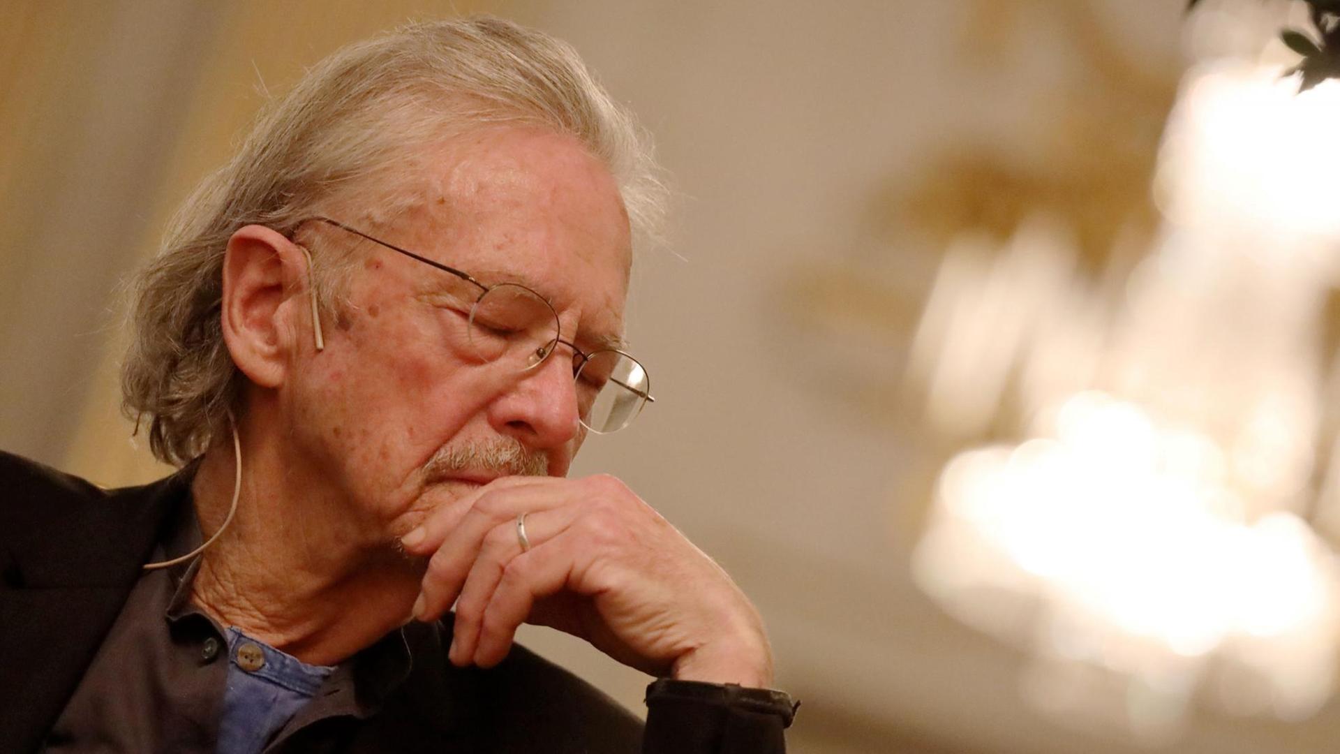 Schriftsteller Peter Handke auf der Pressekonferenz zum Literaturnobelpreis am 5. Dezember in Stockholm. Ein älterer Herr sitzt auf einem Stuhl, hat den Kopf gesenkt und hat die Augen geschlossen. Schriftsteller Peter Handke auf der Pressekonferenz zum Literaturnobelpreis am 5. Dezember in Stockholm. Ein älterer Herr sitzt auf einem Stuhl, hat den Kopf gesenkt und hat die Augen geschlossen.